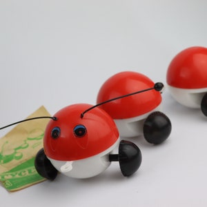 Peut inclure: Trois insectes jouets rouges et blancs avec des roues et des yeux noirs. Les insectes sont reliés par une ficelle noire.