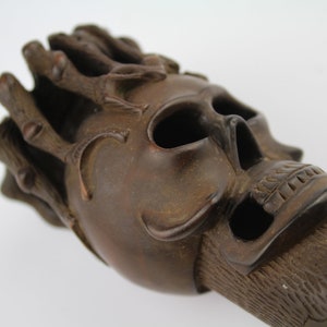 Könnte beinhalten: Eine dunkelbraune Holzskulptur eines Schädels mit aufwendigen Details. Der Schädel hat eine Dornenkrone oben und ein detailliertes Gesicht mit einem geschnitzten Mund und Augen.