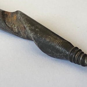 May include: Close-up of a rusty, metal drill bit with a pointed tip. The drill bit is designed for drilling into wood or metal.