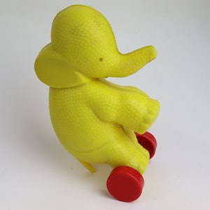 May include: A yellow plastic toy elephant on wheels. The elephant has a textured surface and red wheels.