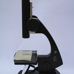 May include: A black microscope with a stage and a mirror. The microscope has a label that reads "УШМ-1 N 8008".