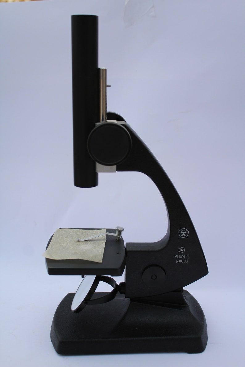 May include: A black microscope with a stage and a mirror. The microscope has a label that reads "УШМ-1 N 8008".