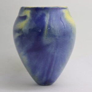 May include: A ceramic vase with a rounded body and a narrow neck. The vase is primarily blue with streaks of yellow and white, creating a marbled effect. The vase is approximately 20 cm tall.