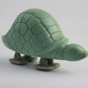 Op de afbeelding: Een groene plastic speelgoed schildpad met een gedetailleerde schild en wielen. De schildpad staat op een witte achtergrond.