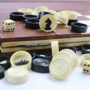 May include: A close-up of a checkers game set with black and white pieces, a white die, and a black knight piece. The game board is closed and the pieces are scattered around it.