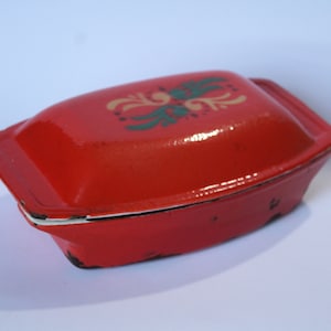May include: Red enamelware casserole dish with a white rim and a floral design in yellow, green, and black.