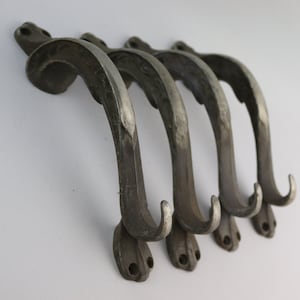 May include: Set of four antique metal hooks with a decorative design. The hooks are silver in color and have a curved shape.