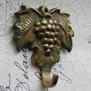 May include: A brass hook shaped like a grapevine with leaves and grapes. The hook is a decorative accent for a home or garden.