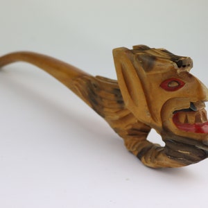 May include: A wooden pipe carved in the shape of a grotesque face with red painted details. The pipe has a long, curved stem.