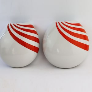 May include: Two white ceramic vases with red and white striped designs. The vases are round and have a smooth, glossy finish.