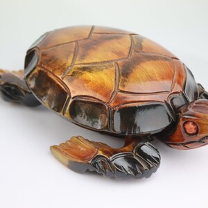 Op de afbeelding: Een handgesneden houten schildpadfiguur met een bruin en zwarte schild en rode ogen. De schildpad bevindt zich in een looppositie met zijn kop naar rechts gedraaid.