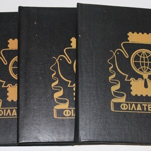 以下が含まれることがあります： 金色の文字とイラストが施された黒いハードカバーの本が3冊。本は「Filatelia」というタイトルで、拡大鏡を持った鳩が描かれている。