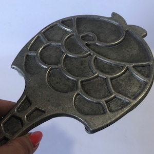 May include: A silver metal waffle iron shaped like a fish with a scalloped design.