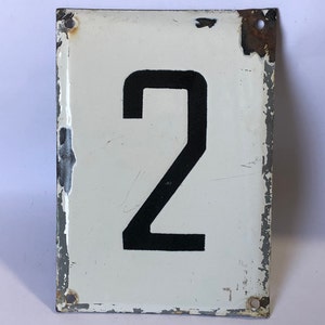 May include: Rectangular white metal sign with the black number 2. The sign has a distressed appearance with chipped paint around the edges and four mounting holes. The sign is likely vintage or antique.