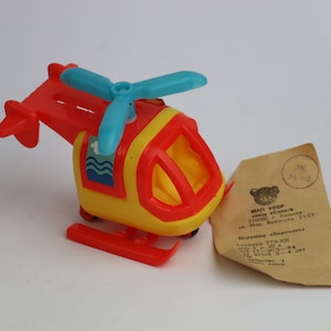 May include: A red, yellow, and blue toy helicopter with a spinning propeller. The helicopter has a small window and a red landing gear. The toy is made of plastic and is in good condition.