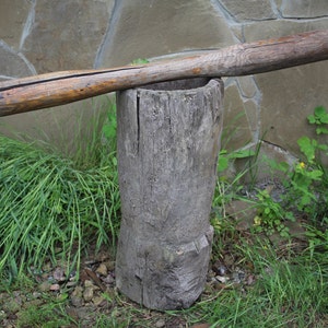 Puede incluir: Un mortero y un pilón de madera, hechos de un tronco de árbol, con un pilón de madera descansando en la parte superior. El mortero y el pilón están sentados sobre un lecho de hierba verde.