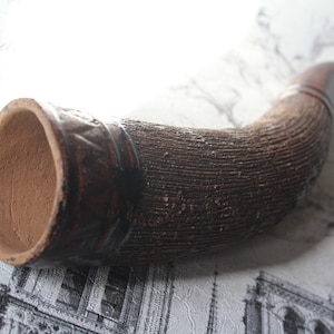 Puede incluir: Un cuerno de cerámica marrón con una superficie texturizada y una abertura ancha en un extremo.