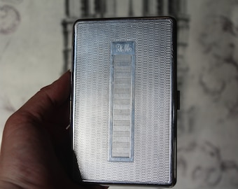 May include: A silver cigarette case with a textured surface and the word "Hello" embossed on the front.