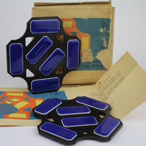 May include: Two sets of blue and black tile-like pieces in a cross shape. The tiles are arranged in a pattern and are used for a game or activity. The tiles are on a yellow and orange paper with text in Russian.