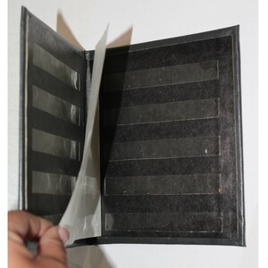 以下が含まれることがあります： 写真を入れるための透明なプラスチック製のシートが付いた黒い写真アルバム。アルバムが開いてシートが見えるようになっています。