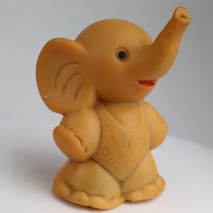 May include: A small, brown rubber toy elephant wearing a patterned swimsuit. The elephant has a long trunk and large ears.
