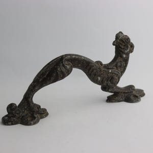 Może przedstawiać: Antyczny, brązowy klamka do drzwi w kształcie stylizowanego smoka z misternymi detalami.