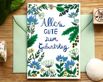 May include: A white card with a blue floral border and the text "Alles Gute zum Geburtstag" in blue lettering.
