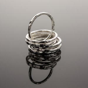 Puede incluir: Una pila de anillos de plata martillados, cada uno con un ancho y una textura ligeramente diferentes. Los anillos est&aacute;n dispuestos en un patr&oacute;n circular, con el anillo m&aacute;s grande en la parte inferior y el anillo m&aacute;s peque&ntilde;o en la parte superior.
