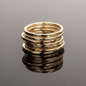 May include: A stack of eight gold hammered rings, each with a slightly different width. The rings are stacked on top of each other, creating a unique and stylish look.