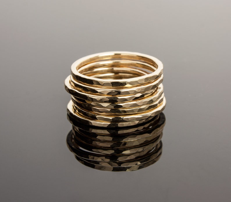May include: A stack of eight gold hammered rings, each with a slightly different width. The rings are stacked on top of each other, creating a unique and stylish look.