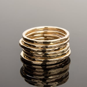May include: A stack of eight gold hammered rings, each with a slightly different width. The rings are stacked on top of each other, creating a textured and unique look.