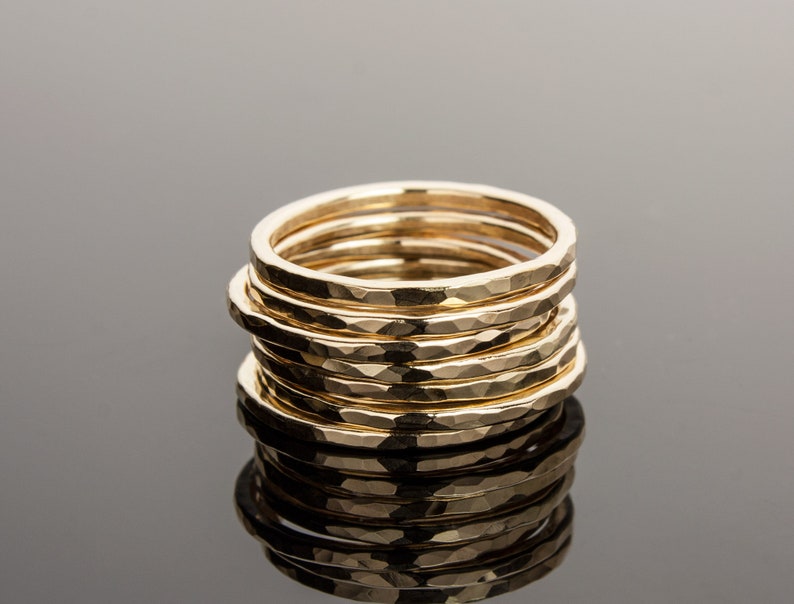 May include: A stack of eight gold hammered rings, each with a slightly different width. The rings are stacked on top of each other, creating a textured and unique look.