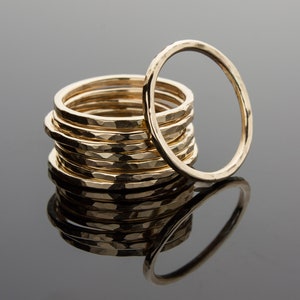 May include: A stack of gold hammered rings, with one ring standing upright in the center. The rings are all the same size and have a hammered texture.