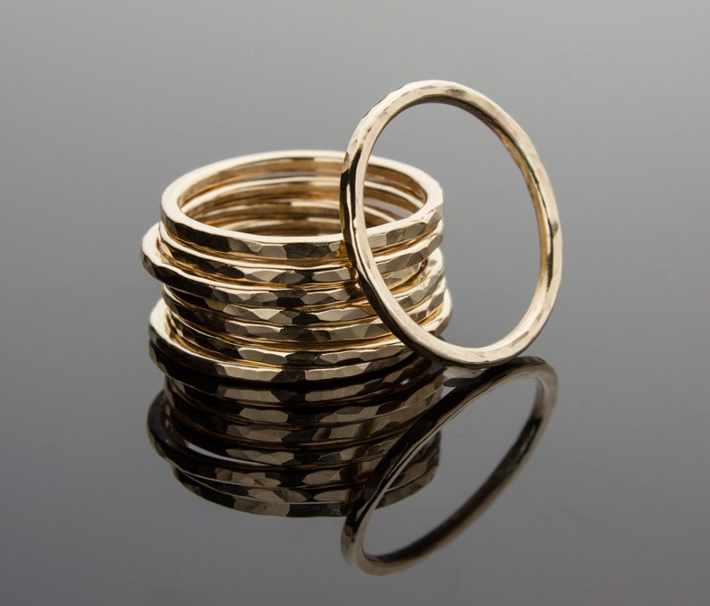 May include: A stack of gold hammered rings, with one ring standing upright in the center. The rings are all the same size and have a hammered texture.