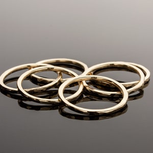 May include: A set of five gold-toned rings with a hammered texture. The rings are stacked on top of each other.