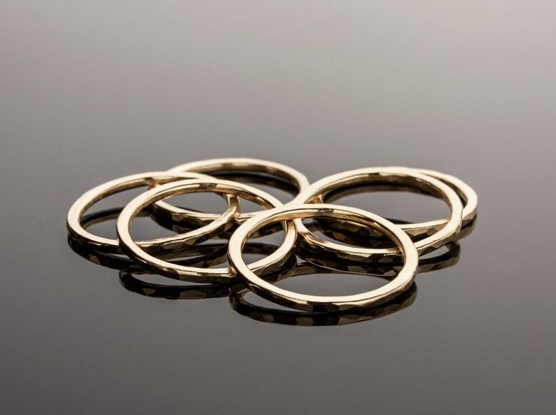 May include: A set of five gold-toned rings with a hammered texture. The rings are stacked on top of each other.