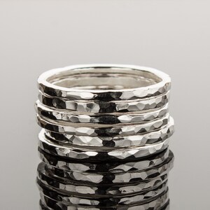 Puede incluir: Una pila de seis anillos de plata martillados. Los anillos tienen todos el mismo ancho y una superficie texturizada.