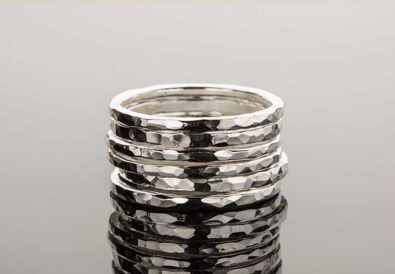 Puede incluir: Una pila de seis anillos de plata martillados. Los anillos tienen todos el mismo ancho y una superficie texturizada.
