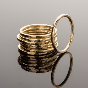 May include: A stack of ten gold hammered rings, with one ring laying on its side in front of the stack.