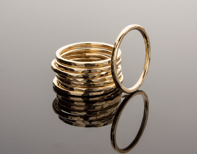 May include: A stack of ten gold hammered rings, with one ring laying on its side in front of the stack.