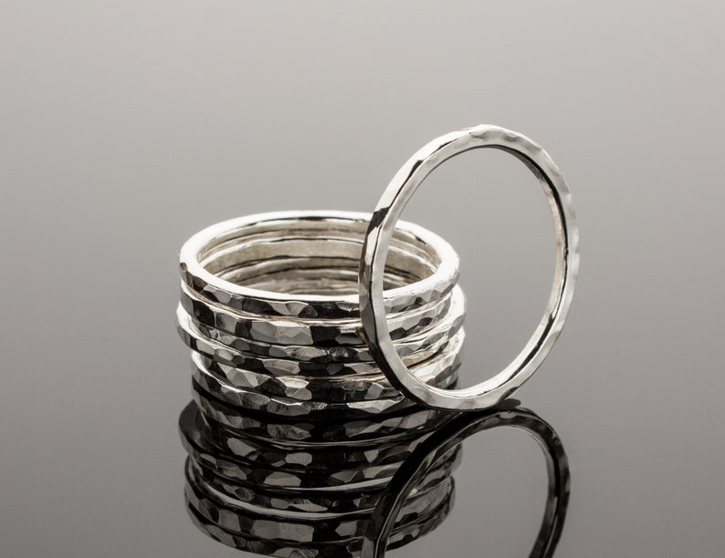 Puede incluir: Una pila de ocho anillos de plata martillados, con un anillo colocado encima de la pila. Los anillos son todos del mismo tama&ntilde;o y tienen una textura martillada.