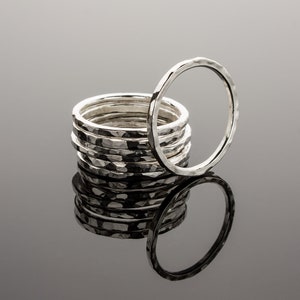 Puede incluir: Una pila de anillos de plata martillados, con un anillo de pie detr&aacute;s de la pila. Los anillos son todos del mismo tama&ntilde;o y tienen una superficie texturizada.