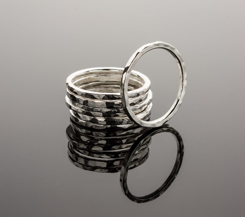 Puede incluir: Una pila de anillos de plata martillados, con un anillo de pie detr&aacute;s de la pila. Los anillos son todos del mismo tama&ntilde;o y tienen una superficie texturizada.