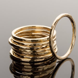 May include: A stack of ten gold hammered rings, with one ring laying beside the stack. The rings are all the same size and have a hammered texture.