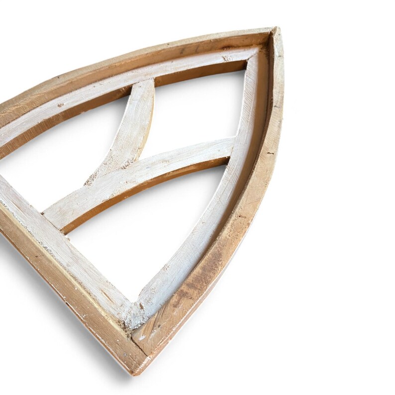 May include: A whitewashed wood arched window frame with a decorative, geometric design. The frame is unfinished and has a rustic, farmhouse style.