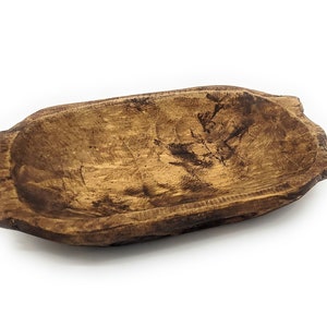 May include: A rustic wooden bowl with a natural brown finish. The bowl has a slightly oval shape and a smooth, worn surface.