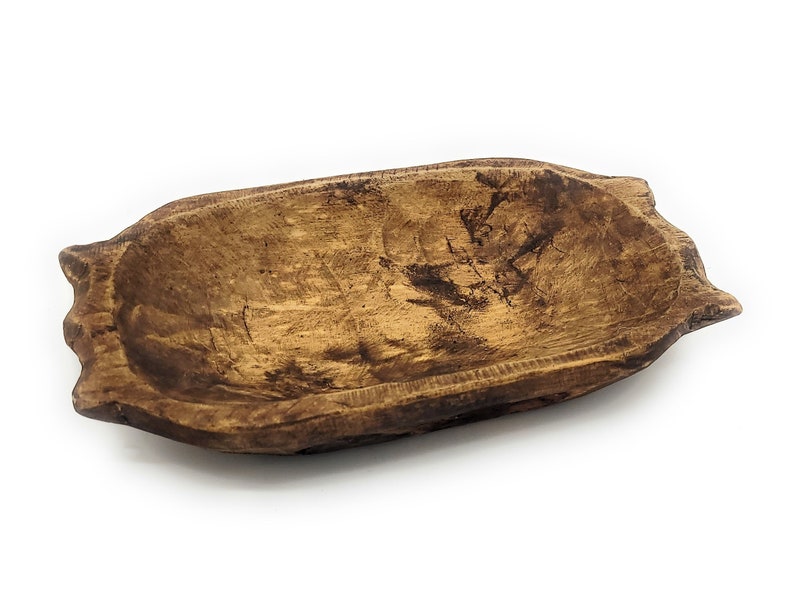 May include: A rustic wooden bowl with a natural brown finish. The bowl has a slightly oval shape and a smooth, worn surface.