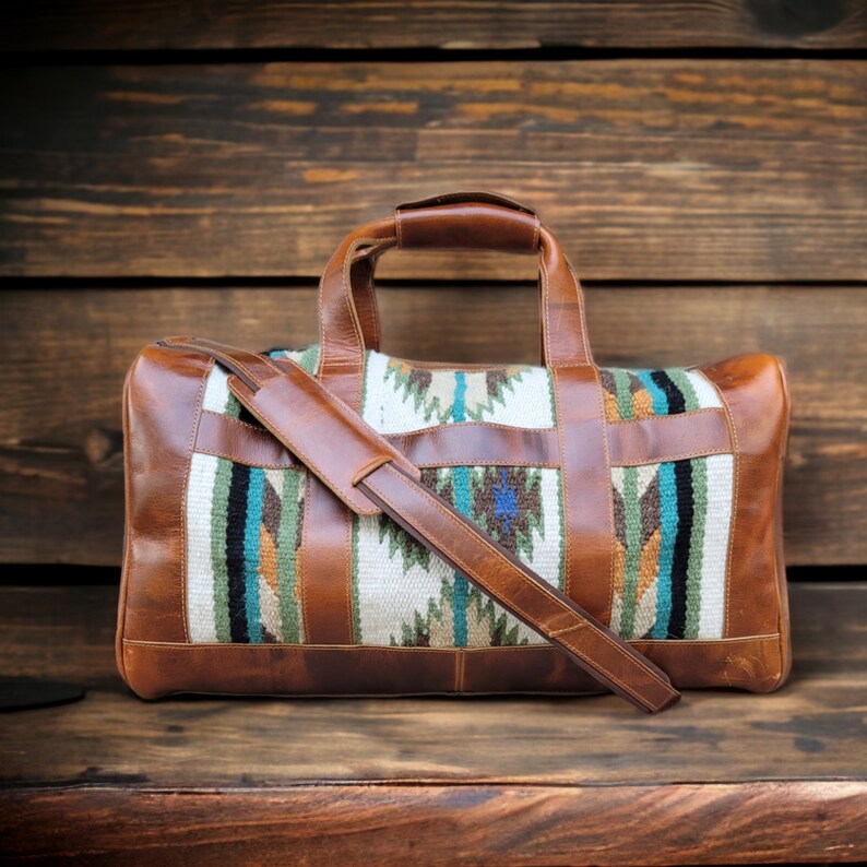 May include: A brown leather duffel bag with a woven pattern in shades of blue, green, and orange. The bag has a long strap and a top handle.