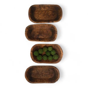 May include: Four wooden bowls of varying sizes, stacked vertically. The top three bowls are empty, while the bottom bowl is filled with small green moss balls.