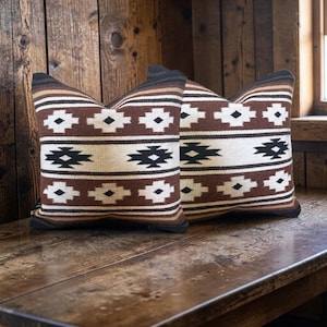 May include: Two square throw pillows featuring a woven geometric pattern in shades of brown, cream, and black. The design consists of horizontal stripes alternating with repeating diamond and cross motifs across the entire surface of the fabric.
